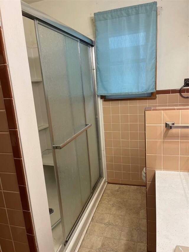 bathroom with a shower with door, tile walls, and toilet