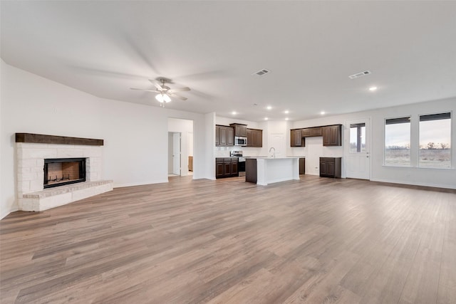 unfurnished living room with light hardwood / wood-style flooring, ceiling fan, and a stone fireplace