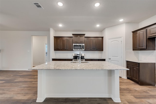 kitchen with a kitchen island with sink, sink, hardwood / wood-style flooring, appliances with stainless steel finishes, and dark brown cabinets