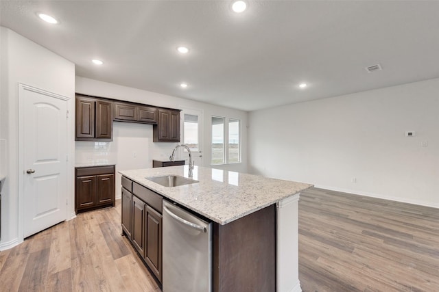 kitchen with light wood-type flooring, light stone counters, stainless steel dishwasher, a kitchen island with sink, and sink