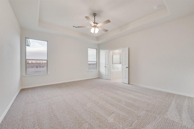 carpeted empty room with a raised ceiling, ceiling fan, and a healthy amount of sunlight