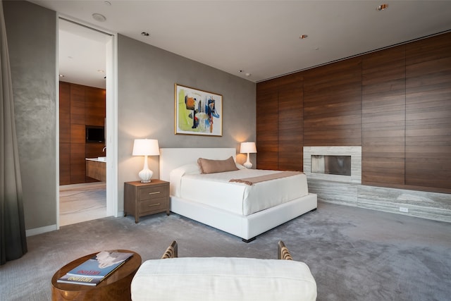 carpeted bedroom with a fireplace, connected bathroom, and wood walls