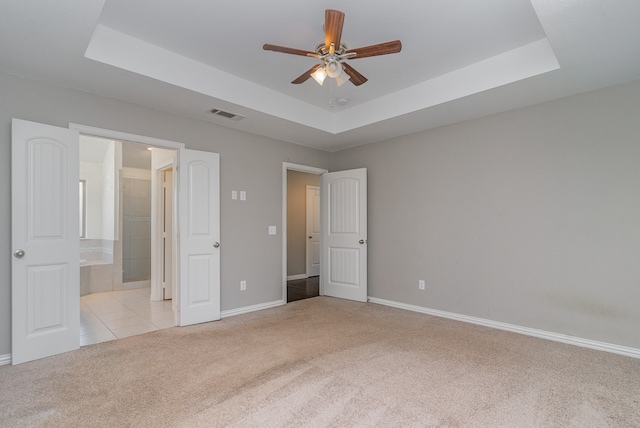 unfurnished bedroom featuring connected bathroom, ceiling fan, a tray ceiling, and light colored carpet