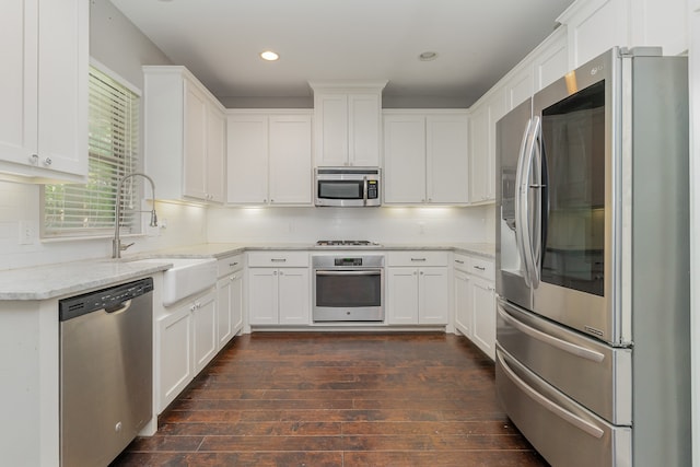 kitchen with appliances with stainless steel finishes, dark hardwood / wood-style floors, white cabinets, and tasteful backsplash