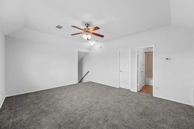 unfurnished bedroom featuring ceiling fan, dark colored carpet, ensuite bathroom, and vaulted ceiling