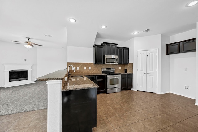 kitchen with appliances with stainless steel finishes, stone countertops, sink, kitchen peninsula, and ceiling fan