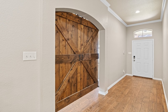 foyer entrance featuring crown molding, a textured ceiling, and light hardwood / wood-style flooring