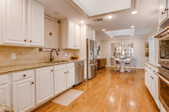 kitchen with white cabinets, a skylight, light hardwood / wood-style flooring, stainless steel appliances, and sink