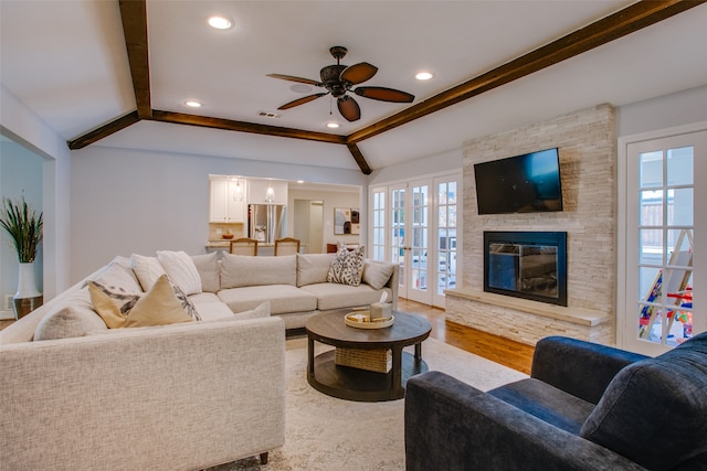 living room with a fireplace, lofted ceiling with beams, french doors, light hardwood / wood-style floors, and ceiling fan