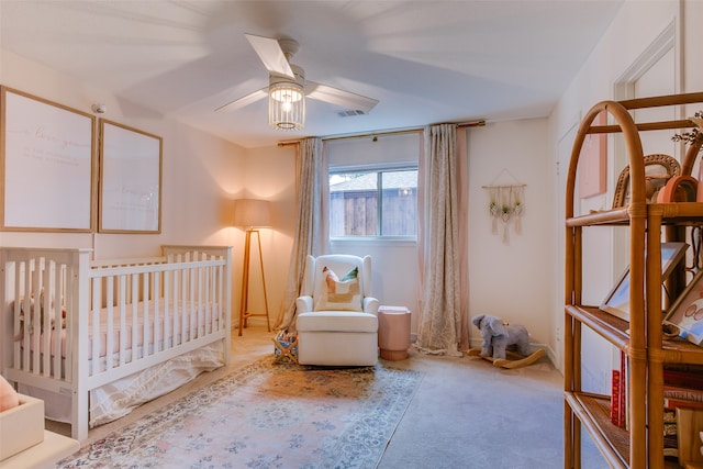 carpeted bedroom featuring ceiling fan and a nursery area