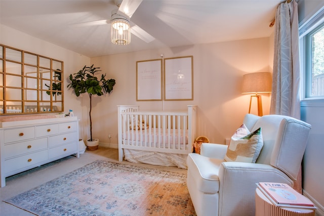 bedroom with light colored carpet, a nursery area, and ceiling fan