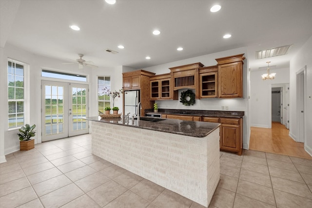 kitchen with black cooktop, ceiling fan with notable chandelier, sink, white refrigerator, and a center island with sink