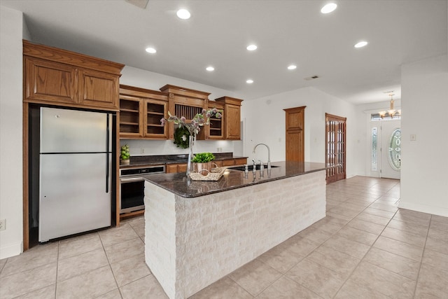 kitchen featuring white fridge, an inviting chandelier, sink, stainless steel oven, and a center island with sink