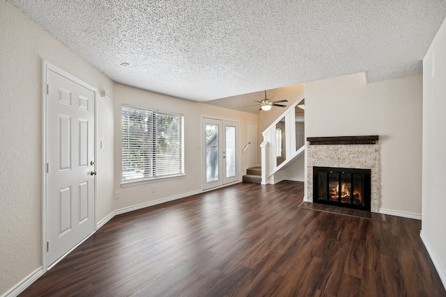 unfurnished living room with a textured ceiling, dark hardwood / wood-style flooring, ceiling fan, and a stone fireplace