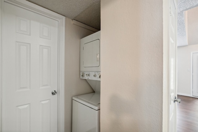 laundry room featuring hardwood / wood-style flooring, stacked washer and dryer, and a textured ceiling