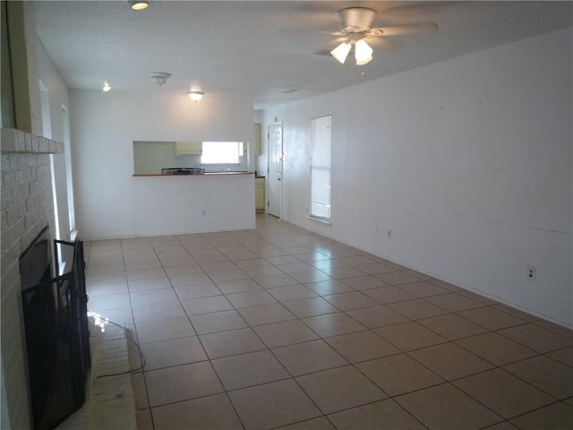 unfurnished living room featuring a brick fireplace, light tile patterned floors, and ceiling fan