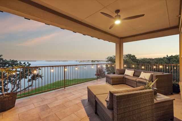 patio terrace at dusk featuring a balcony, a water view, ceiling fan, and outdoor lounge area