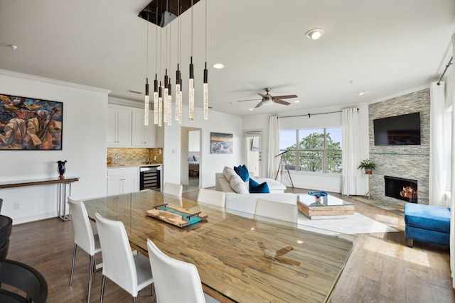 dining area with ceiling fan, wine cooler, ornamental molding, dark hardwood / wood-style floors, and a fireplace