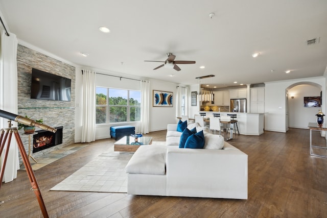 living room with wood-type flooring, a stone fireplace, ornamental molding, and ceiling fan