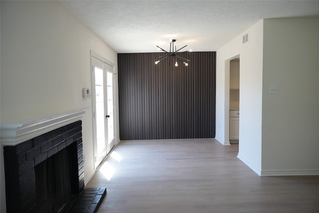 unfurnished living room with a fireplace, hardwood / wood-style flooring, a textured ceiling, and a chandelier