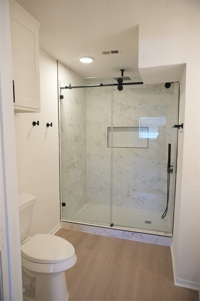 bathroom featuring wood-type flooring, toilet, a textured ceiling, and a shower with shower door