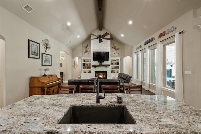 kitchen featuring vaulted ceiling with beams, visible vents, open floor plan, a sink, and a stone fireplace