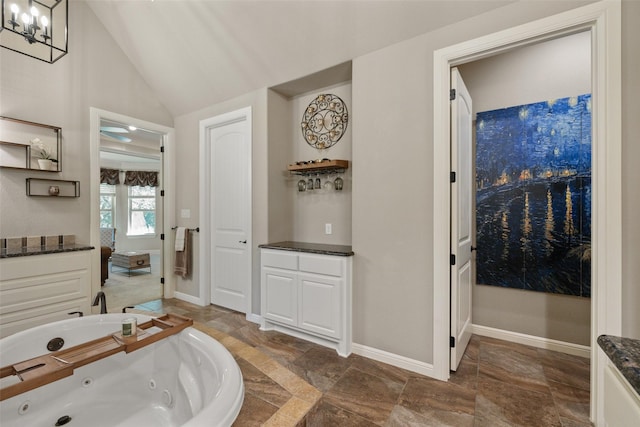 full bathroom featuring a chandelier, baseboards, vaulted ceiling, a tub with jets, and stone finish floor