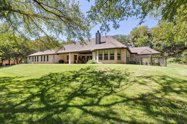 rear view of house featuring brick siding, a lawn, and a chimney