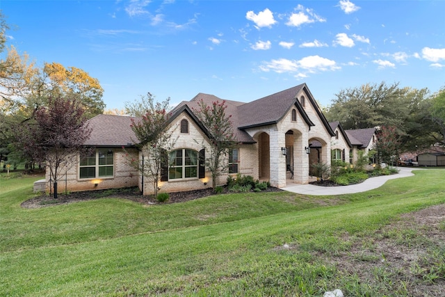 french country inspired facade featuring stone siding, a shingled roof, brick siding, and a front yard