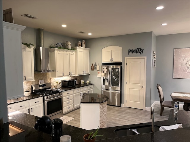 kitchen with stainless steel appliances, wall chimney range hood, light wood-type flooring, and white cabinetry