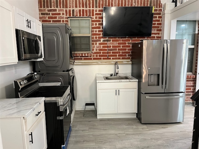 kitchen featuring appliances with stainless steel finishes, brick wall, stacked washer and clothes dryer, and white cabinets