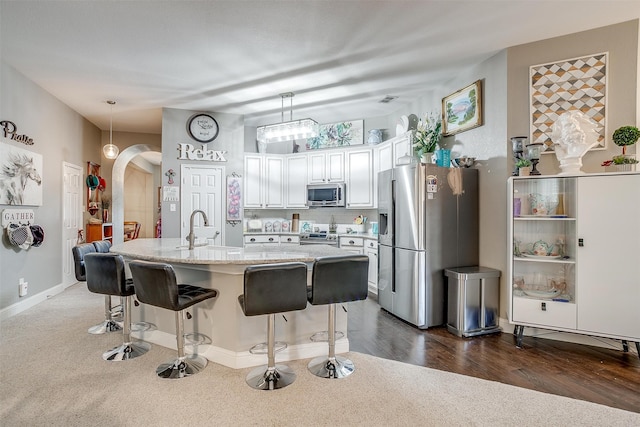 kitchen with dark hardwood / wood-style floors, appliances with stainless steel finishes, a kitchen bar, hanging light fixtures, and white cabinetry