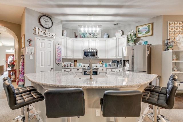 kitchen with light wood-type flooring, hanging light fixtures, white cabinetry, stainless steel appliances, and a breakfast bar