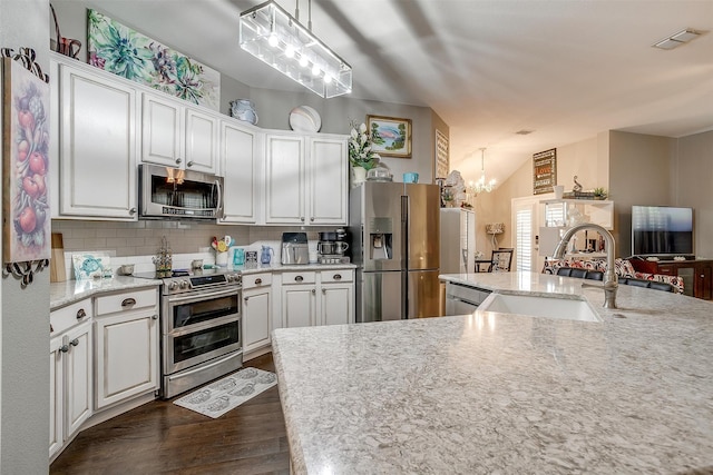 kitchen with appliances with stainless steel finishes, a chandelier, white cabinets, and pendant lighting