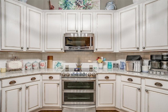 kitchen featuring backsplash, light stone countertops, appliances with stainless steel finishes, and white cabinetry