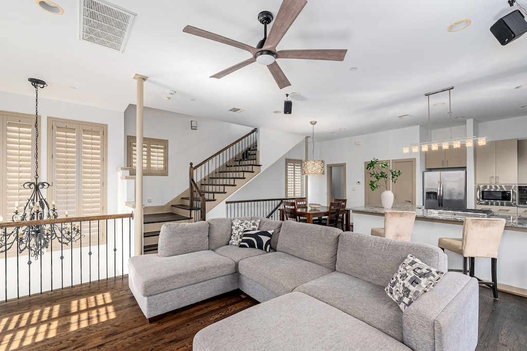 living room with ceiling fan with notable chandelier and dark hardwood / wood-style flooring