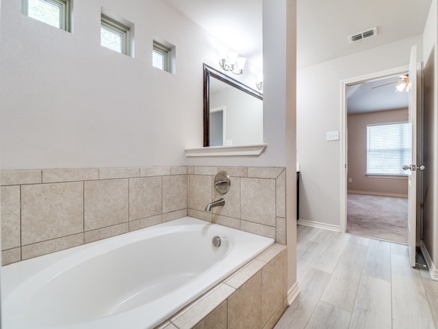 bathroom with a wealth of natural light, tiled tub, and hardwood / wood-style floors