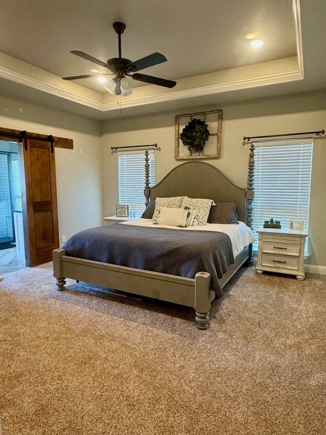 carpeted bedroom featuring a tray ceiling, crown molding, ceiling fan, and a barn door