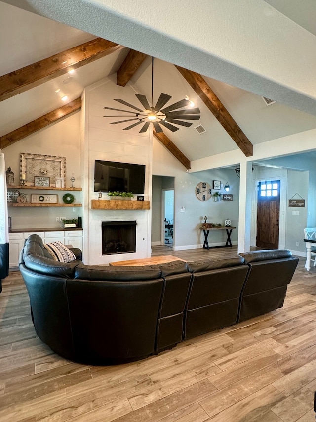 living room featuring ceiling fan, hardwood / wood-style flooring, a fireplace, and lofted ceiling with beams