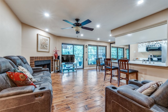 living room featuring ceiling fan, a brick fireplace, and light hardwood / wood-style floors