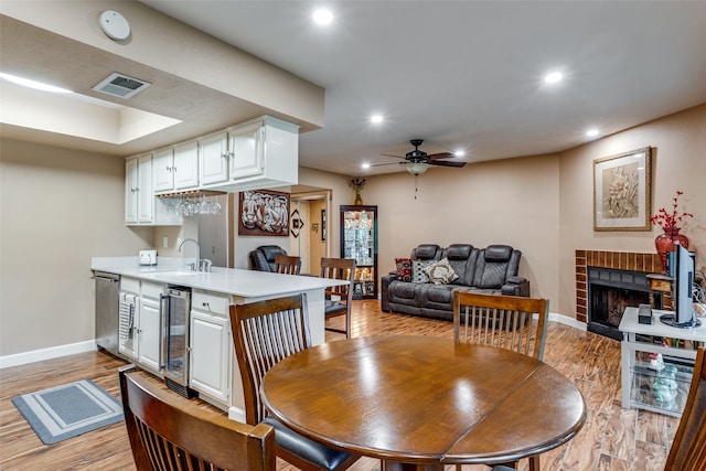 dining room featuring ceiling fan, sink, a brick fireplace, beverage cooler, and light hardwood / wood-style floors