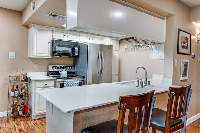 kitchen with appliances with stainless steel finishes, kitchen peninsula, white cabinetry, and a kitchen breakfast bar