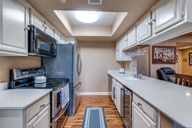 kitchen featuring light wood-type flooring, beverage cooler, white cabinetry, a raised ceiling, and appliances with stainless steel finishes