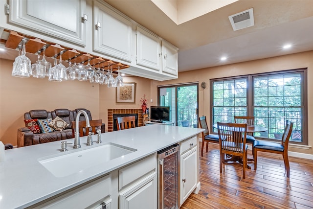 kitchen featuring light wood-type flooring, wine cooler, sink, white cabinetry, and a fireplace