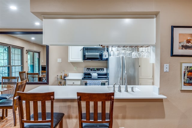 kitchen featuring a kitchen breakfast bar, light hardwood / wood-style floors, white cabinets, stainless steel appliances, and sink