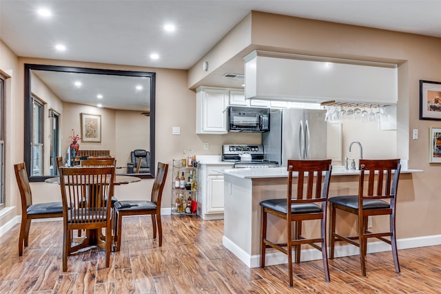 kitchen featuring light hardwood / wood-style flooring, white cabinetry, kitchen peninsula, and appliances with stainless steel finishes