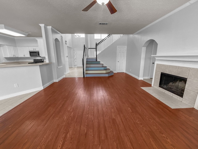 unfurnished living room featuring light wood-type flooring, crown molding, a textured ceiling, a tile fireplace, and ceiling fan