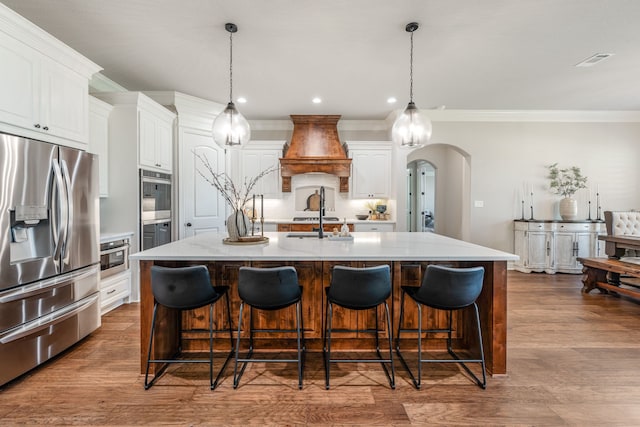 kitchen featuring decorative light fixtures, custom exhaust hood, white cabinetry, stainless steel refrigerator with ice dispenser, and a kitchen island with sink