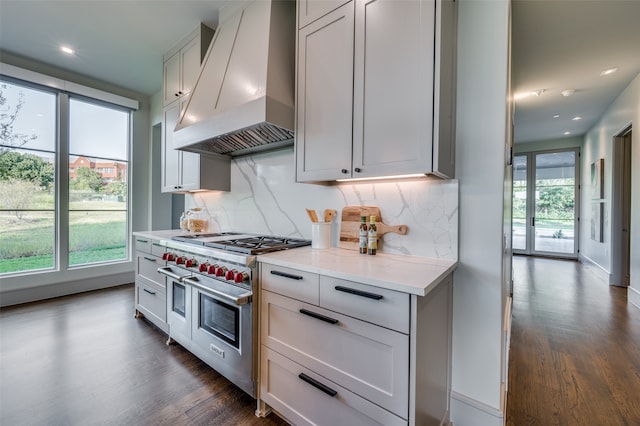 kitchen with light stone counters, dark wood-type flooring, custom exhaust hood, decorative backsplash, and range with two ovens