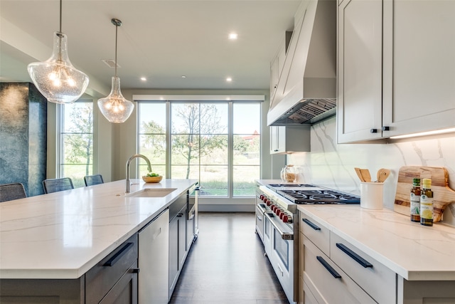 kitchen with hanging light fixtures, a kitchen island with sink, custom exhaust hood, and stainless steel appliances